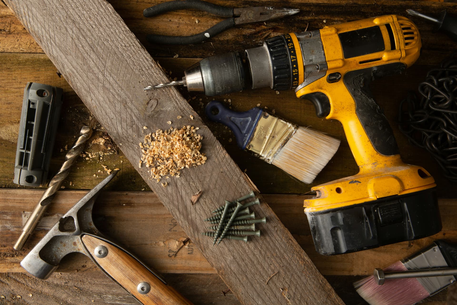 Cordless drill, hammer, paintbrush and screws on a timber workbench